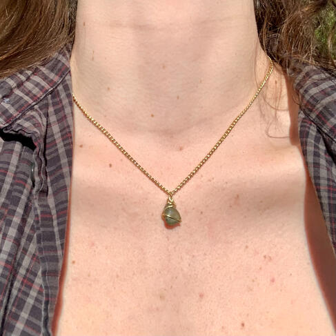 A person's collarbone area showcasing a necklace with a gold chain and a green stone.
