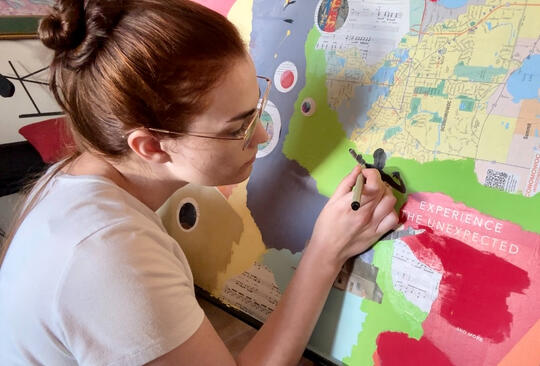The artist draws on a small area of a large mixed media piece.